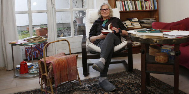 Eine Frau sitzt im Wohnzimmer auf einem Sessel und blättert in einem Buch