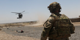 Ein US-Soldat steht mit dem Rücken zur Kamera in der Wüste in Afghanistan. Er beobachtet einen Hubschrauber, der gerade landet