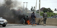 Drei Polizisten auf einer Straße in Abuja. Sie schlagen auf ein Feuer ein, um es zu löschen