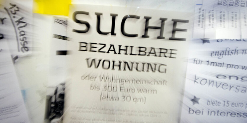 Eine Suchanzeige für eine "bezahlbare Wohnung" hängt an einem schwarzen Brett.