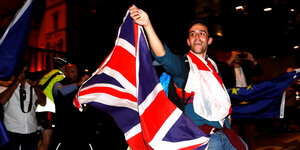 Ein Anti-Brexit-Demonstrant tanzt nachts. In einer Hand hält er eine britische, in der anderen eine EU-Flagge