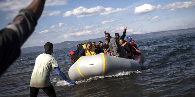 Flüchtende Menschen sitzen in einem überfüllten Schlauchboot, das an der Insel Lesbos in Griechenland ankommt. Ein Mann steht im Wasser und nimmt sie in Empfang