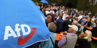 Ein Volksfest. Menschen sitzen auf Bierbänlen. Im Vordergrund steht ein Sonnenschirm von der Alternativen für Deutschland AfD.