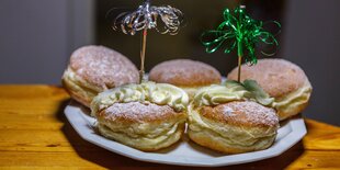 Mehrere Berliner, auch Pfannkuchen genannt, liegen auf einem Teller, zwei sind mit Dekospießchen versehen