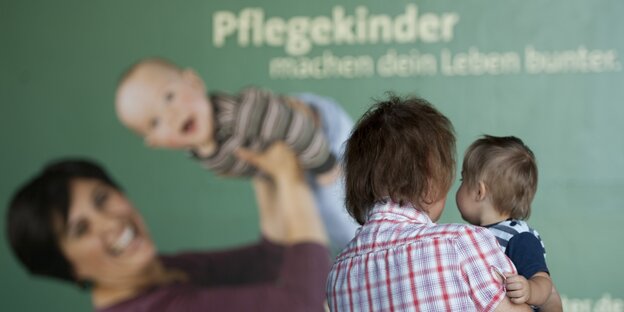 Eine Frau mit Kind steht vor einem Plakat des Kinder- und Jugendhilfeverbundes.