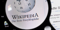 Jemand hält eine Lupe vor den Bildschirm eines Computers, auf dem die Seite Wikipedia aufgerifen ist.