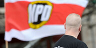 Eine NPD-Fahne weht im Wind. Vor ihr ein Mann mit kurzgeschorenen Haaren