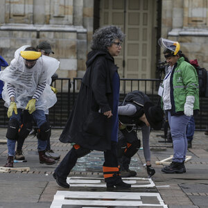 Doris Salcedo schreitet über den Platz Plaza Bolivar in Botoa. Im Hintergrund sind Aktivistinnen und Aktivisten, die an „Quebrantos“ (Brüche) arbeiten. Sie zerbrechen Glas und tragen Schutzkleidung. Doris Salcedo schreitet über den Platz Plaza Bolivar in Botoa. Im Hintergrund sind Aktivistinnen und Aktivisten, die an „Quebrantos“ (Brüche) arbeiten. Sie zerbrechen Glas und tragen Schutzkleidung.