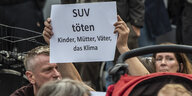 Teilnehmer der Mahnwache, bei der der Verkehrstoten gedacht wird, stehen mit einem Schild mit der Aufschrift "SUV töten Kinder, Mütter, Väter, das Klima". An der Stelle waren am Freitag vier Menschen bei einem Verkehrsunfall gestorben