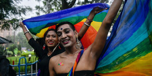 Zwei LGBTQI-Aktivist*innen halten eine Regenbogenfahne hoch
