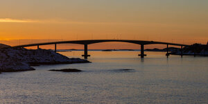Sonnenuntergang hinter der Sommaroy-Brücke unter, die die Inseln Kvaloya und Sommaroy verbindet. Fast alle Brücken in Norwegen sind mautpflichtig