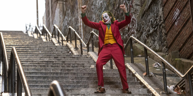 Joaquin Phoenix verkleidet als der Joker von Batman. Er steht auf einer Treppe und tanzt.