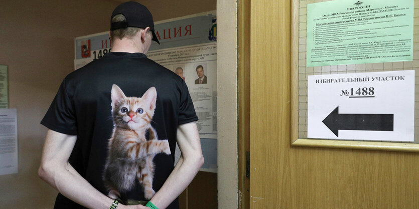 Ein Mann mit einer großen Katze als Motiv auf dem Rücken seines T-Shirts geht in ein Wahlbüro in Moskau