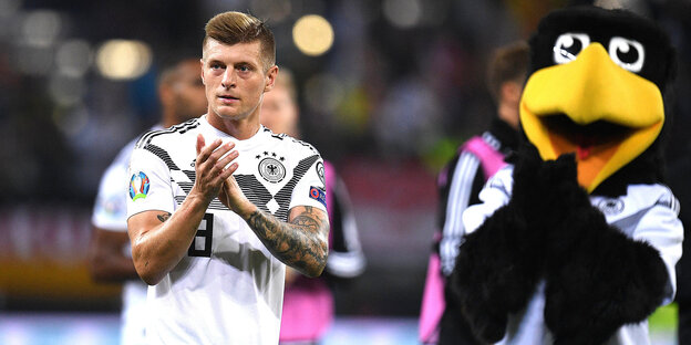 Ein Mann im deutschen Trikot und das Maskottchen der deutschen Fußballmannschaft der Männer, ein großer Rabe, applaudieren nach dem Spiel.