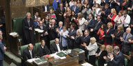 Abgeordnete im britischen Unterhaus applaudieren stehend für einen Mann in einem Talar, der vor ihnen steht. Der Mann im Talar ist der Präsident des Parlaments.