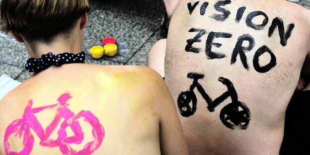 Zwei Menschen auf deren Rücken mit Farbe ein Fahrrad gemalt wurde, auf einem Rücken steht Vision Zero
