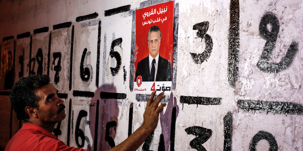 Mann in Tunis hängt ein Wahlplakat auf, es zeigt Nabil Karoui