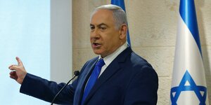 Benjamin Netanjahu steht an einem Rednerpult und zeigt nach rechts