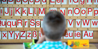 Ein Junge sitzt vor einer Wand, an der das Alphabet aufgereiht ist.