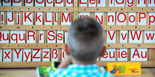 Ein Junge sitzt vor einer Wand, an der das Alphabet aufgereiht ist.