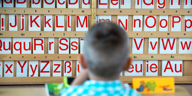 Ein Junge sitzt vor einer Wand, an der das Alphabet aufgereiht ist.