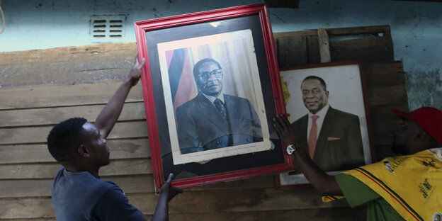 Ein Mann hängt ein Bild mit Robert Mugabe auf, cdireketdneben dem Portrait des derzeitigen Präsidenten, Emmerson Mnangagwa.
