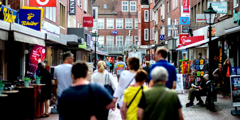 Passanten gehen durch die Fußgängerzone im Zentrum von Emden, Niedersachsen. Sie sind von hinten zu sehen.