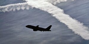 Ein Flugzeug startet vom Flughafen vor zwei Kondensstreifen am Himmel, die sich kreuzen