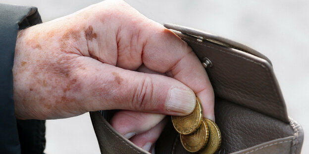 Die Hand eines Seniors hält die letzten Münzen aus einem Ledergelbeutel über dem Münzfach