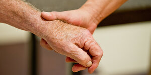 Eine Altenpflegerin hält die Hand eines Mannes.