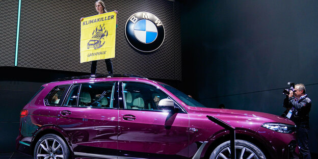 Nach dem Er·öffnungsrundgang von Bundeskanzlerin Merkel (CDU) auf der IAA steht am Stand von BMW eine Aktivistin der Umweltschutzorganisation Greenpeace mit einem Transparent mit der Aufschrift "Klimakiller" auf einem SUV.