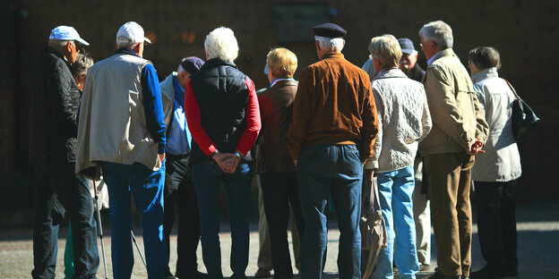 Eine Gruppe von Senioren steht im Kreis in der Sonne wir sehen ihre Rücken