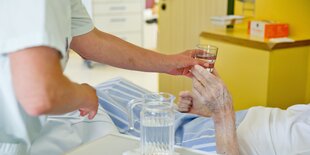 Eine Krankenpflegerin reicht einem Patienten in einem Klinikum ein Glas Wasser.