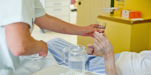 Eine Krankenpflegerin reicht einem Patienten in einem Klinikum ein Glas Wasser.