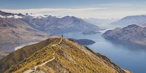 En Wanderer steht an auf einer Bergspitze mit Blick auf eine phanatstsiche Seenlandschaft