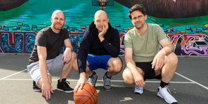 Drei Männer hocken auf einem Basketballfeld