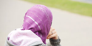 Eine junge Muslimin trägt ein lila Kopftuch zu einem grauen Kapuzenpullover.
