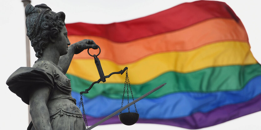 Eine Regenbogenfahne weht hinter der Bronzestatue der Justitia