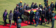 Zahlreiche Menschen in Uniform laufen neben Mugabes Sarg. Auf dem Rasen ist ein roter Teppich ausgerollt