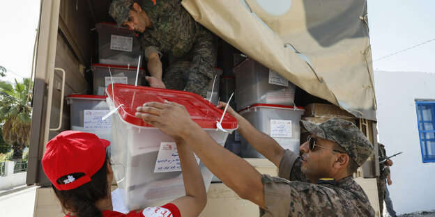 Zwei Soldaten helfen einer Frau, Wahlmaterial aus einem Lastwagen herauszunehmen
