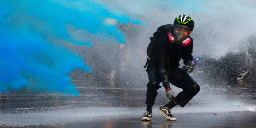 Ein Demonstrant mit Gasmaske wird mit einer blauen Flüssigkeit