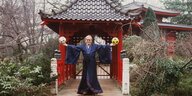 Ein Mann in einem Kimono hält je einen Ball in der Hand und steht in einem japanischen Garten