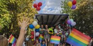 Zu sehen ist ein Demowagen auf der Pride Parade in Berlin, davor stehen viele Menschen mit Regenbogenflaggen