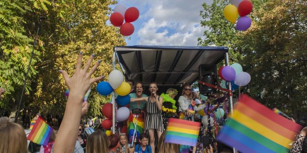 Zu sehen ist ein Demowagen auf der Pride Parade in Berlin, davor stehen viele Menschen mit Regenbogenflaggen