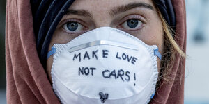 Eine Frau trägt eine Atemmaske auf der Make Love not cars steht