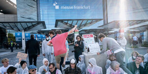 Demonstrantinnen in weißen Kitteln blockieren lachend den Eingang zur Frankfurter Messe. Einige Besucher versuchen darüber zu steigen