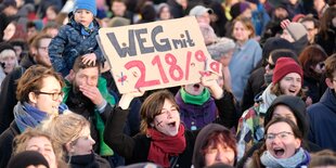 In einer Menschenmenge hält eine Demonstrantin ein Schild hoch mit der Aufschrift "Weg mit 218/9a".