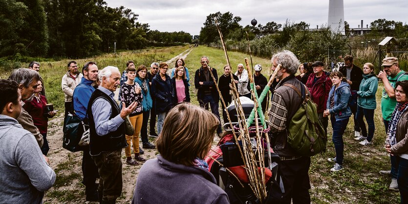 Eine Gruppe Menschen steht vor dem Vollhöfner Wald und hört einem Mann zu, der spricht.