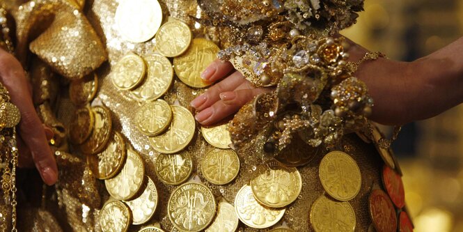 Frauenhände stemmen sich gegen eine Hüfte, die Person trägt ein mit Goldstücken besetztes Kleid