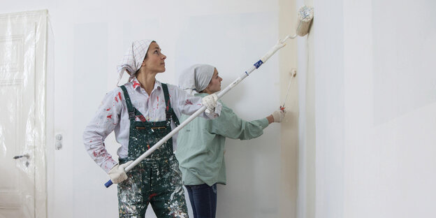 Zwei Menschen streichen eine Wand mit weißer Farbe.